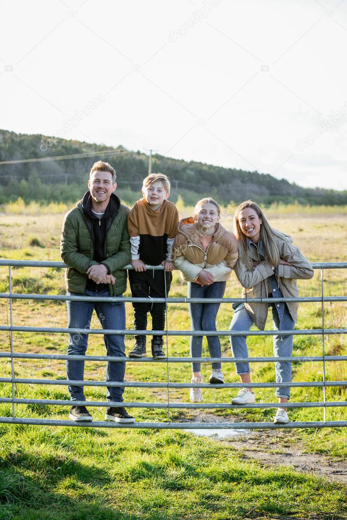 A front-view shot of a caucasian mother and father with their son and daughter, they're all smiling and looking at the camera, while wearing casual clothing for a walk outdoors.