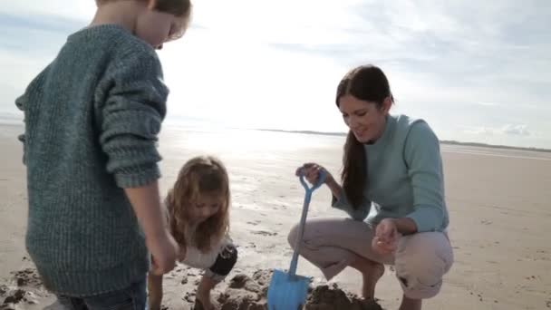 Mor gräva med barnen på stranden — Stockvideo