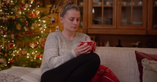 Mulher Relaxando em um sofá Segurando Caneca e Beba Chá Quente na Noite de Natal. — Vídeo de Stock