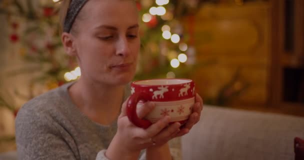 Mulher Relaxando em um sofá Segurando Caneca e Beba Chá Quente na Noite de Natal. — Vídeo de Stock