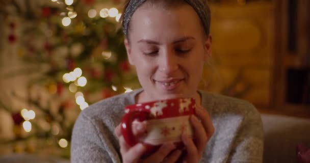 Kobieta Relaks na kanapie trzymając kubek i pić gorącą herbatę w Boże Narodzenie wieczorem. — Wideo stockowe