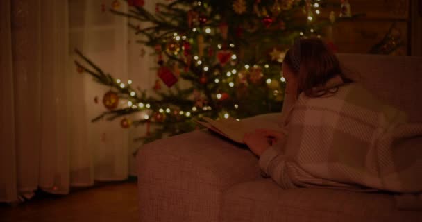 Женщина читает книгу, лежащую на диване в гостиной — стоковое видео