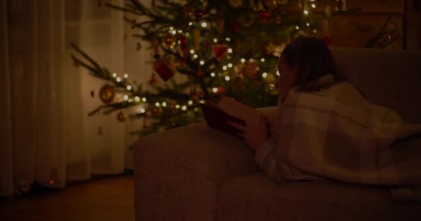 Женщина читает книгу, лежащую на диване в гостиной — стоковое видео