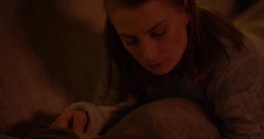 Oturma odasında, koltukta uzanmış kitap okuyan kadın.