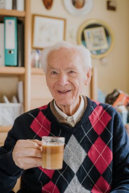 Yaşlı adam evde kahve içiyor.
