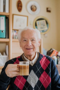 Yaşlı adam evde kahve içiyor.