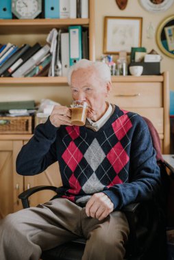 Yaşlı adam evde kahve içiyor.