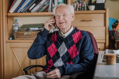 Telefonda konuşan yaşlı bir adam evde oturuyor.