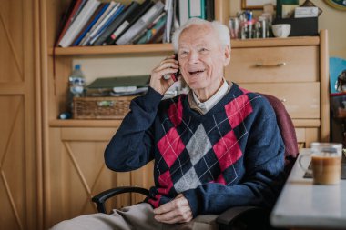 Telefonda konuşan yaşlı bir adam evde oturuyor.