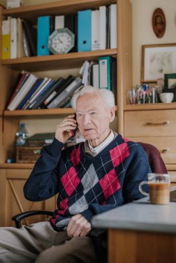 Telefonda konuşan yaşlı bir adam evde oturuyor.