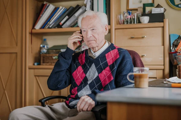 Telefonda konuşan yaşlı bir adam evde oturuyor.