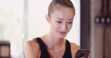 Spor salonunda akıllı telefon kullanan genç kadın.