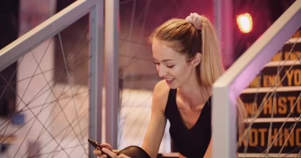 Fit junge Frau nutzt Smartphone im Fitnessstudio — Stockvideo