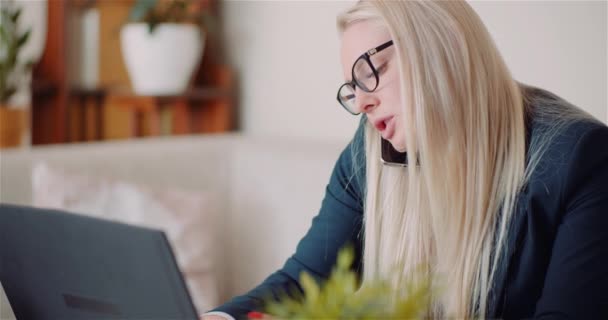 Деловая женщина, работающая над ноутбуком над проектом в Home Office во время разговора с клиентом на мобильном телефоне. — стоковое видео