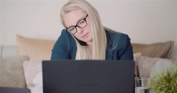 Empresária trabalhando no laptop em um projeto no Home Office enquanto conversa no celular com o cliente. — Vídeo de Stock