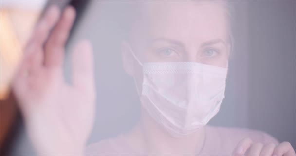 Κοντινό πλάνο πορτρέτο της γυναίκας που φοράει μάσκα δει μέσα από το παράθυρο κατά τη διάρκεια της επιδημίας coronavirus — Αρχείο Βίντεο