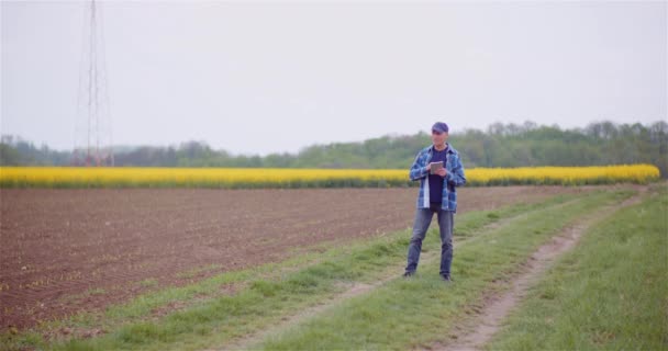 Agricultor examinando el campo agrícola mientras trabaja en la computadora digital de la tableta en la granja. — Vídeo de stock