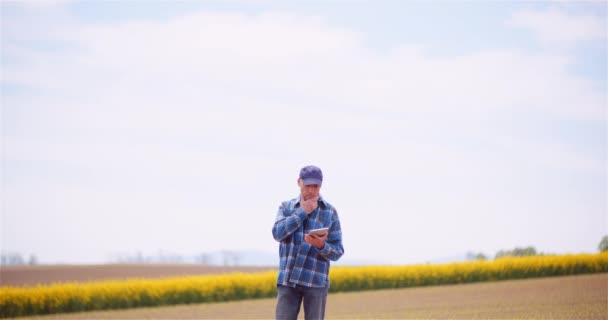 Agricultor examinando el campo agrícola mientras trabaja en la computadora digital de la tableta en la granja. — Vídeo de stock