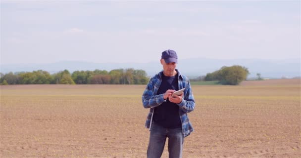 Agricultor examinando el campo agrícola mientras trabaja en la computadora digital de la tableta en la granja. — Vídeo de stock