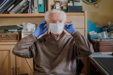 Yaşlı adam koruyucu maske ve eldiven takıyor.