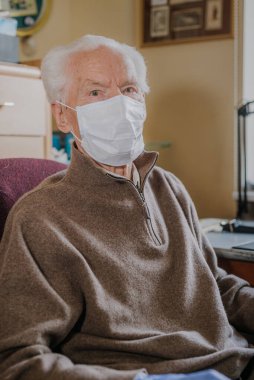 Yaşlı adam koruyucu maske ve eldiven takıyor.