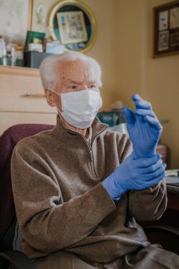 Yaşlı adam koruyucu maske ve eldiven takıyor.