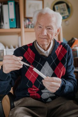 Yaşlı adam termometreyi elinde tutuyor..