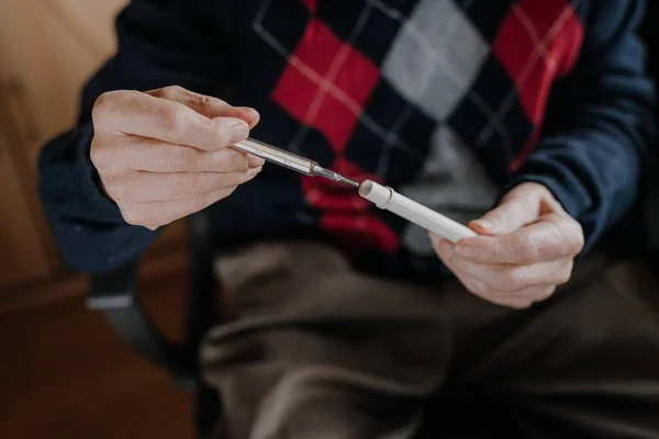 Yaşlı adam termometreyi elinde tutuyor..