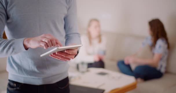 Mann nutzt digitales Tablet im Büro, während zwei Frauen über Projekt diskutieren. — Stockvideo