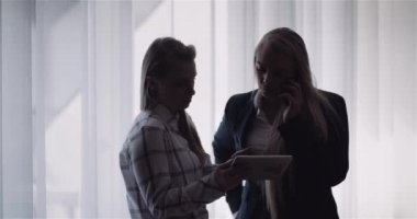 İki kadın tablet görüntüden bahsederken, bir kadın da akıllı telefondan konuşuyor.