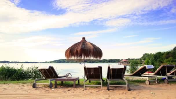 Ligstoelen en parasols bij de oever van het meer — Stockvideo