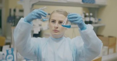 A focused female scientist analyzing material samples in test tubes against a lab background conducting research.
