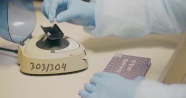 Focused laboratory worker in protective gear evaluates test tubes, analyzing current disease research.