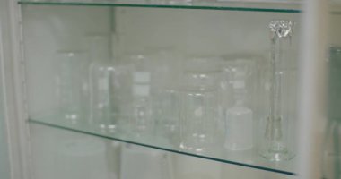 A laboratory worker places clean beakers on a shelf in a laboratory environment.