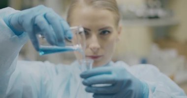 A woman scientist pours material into a beaker in a laboratory setting, conducting medical research.