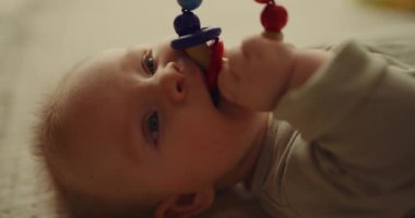 Close-up of a happy newborn baby biting a toy on a blanket, showing emotions with an eco-friendly wooden toy.
