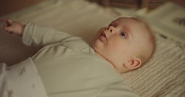 A small baby boy lying on a blanket trying to make eye contact with his parent.