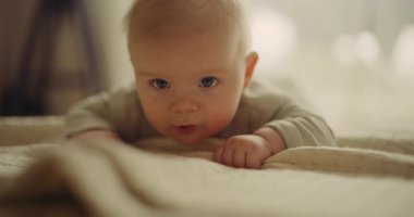 Close-up of a tiny baby who is beginning to crawl for the first time, learning and looking at the camera. Absolutely adorable and very beautiful.