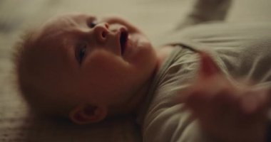 A close-up shot of a newborn baby boy, upset and crying from stomach pain, lying on a blanket.