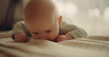 Heartwarming moment of a baby learning to crawl for the first time. The baby moves forward while holding onto a blanket and looks at the camera.