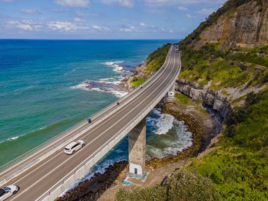 Ünlü Sea Cliff Köprüsü 'nün insansız hava aracı fotoğrafı ve Avustralya' nın Yeni Güney Galler bölgesinin Illawarra bölgesinde güneşli bir pazar günü dalgalarla kıyıya vuran yerel uçurum manzarası.