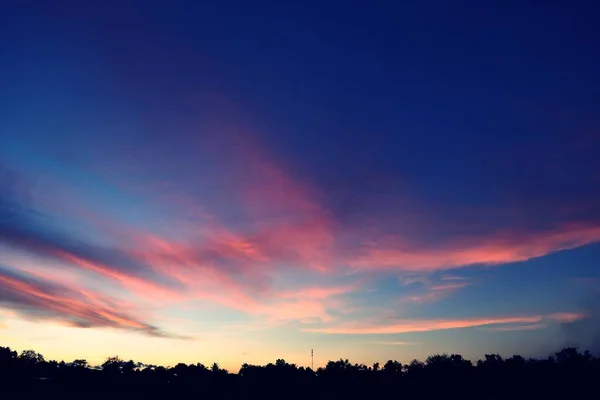 夕阳西下 美丽的蓝天映衬着树木的轮廓 地平线上的光带着紫色和粉色的云彩开始变成橙色 — 图库照片