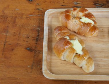 Tereyağlı iki taze kruvasan, kahverengi ahşap masada Fransız ekmeği.