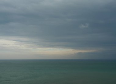 Arka planda mavi gökyüzü ve koyu bulutlu deniz, gölde yeşil suya yağan yağmur.