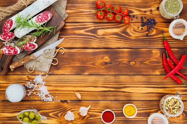 Sliced cured sausage with spices and a sprig of rosemary on wooden rustic background.