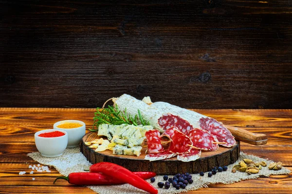 Sliced cured sausage with spices and a sprig of rosemary on dark wooden rustic background.