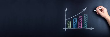 Tebeşirle bir adamın eli tahtaya ekonomik büyüme grafiği çizer.