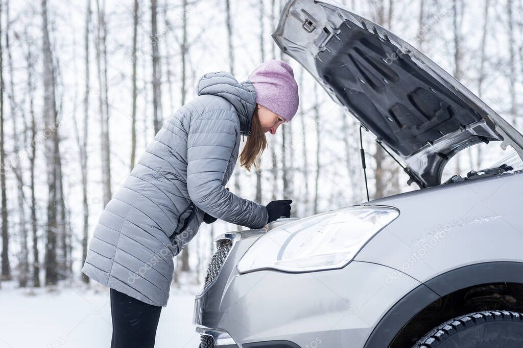 car repair on the road in winter. young girl is trying to fix a car breakdown under the soot on the road. woodsroadside assistance car