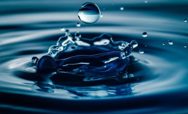Koyu mavi su damlacıkları su yüzeyine yakından sıçradı. Bir su dalgası ve mükemmel bir taç yaratır..