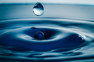 Koyu mavi su damlacıkları su yüzeyine yakından sıçradı. Bir su dalgası ve mükemmel bir taç yaratır..